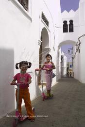 Image du Maroc Professionnelle de  Deux jeunes filles jouent avec leur trottinette dans une rue de la Kasbah d'Asilah, ville du nord du Maroc sur l'océan Atlantique à 40 km au sud de Tanger, Dimanche 9 Septembre 2001 (Photo / Abdeljalil Bounhar)
